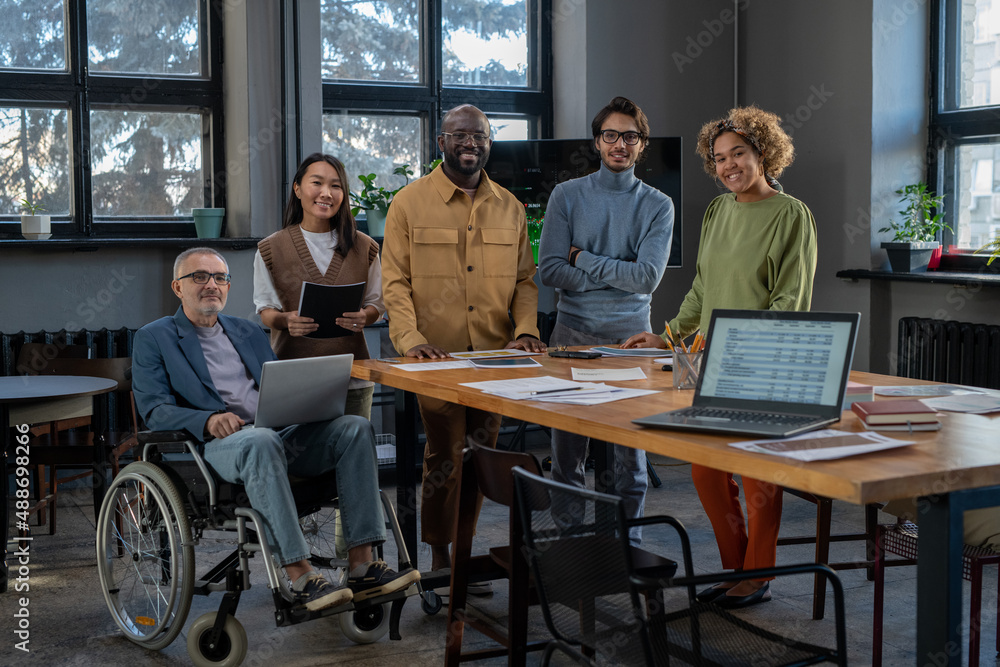 Poster cheerful economists of various ethnicities gathered by workplace looking at camera with smiles while