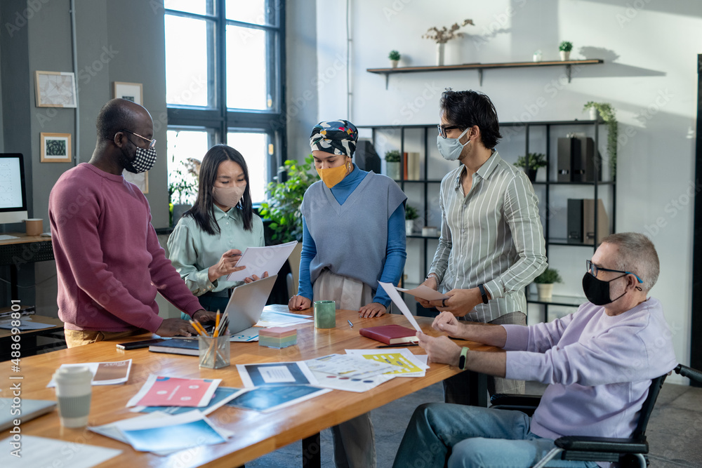Aufkleber Group of contemporary employees in protective masks discussing financial documents while gathered by table for working meeting