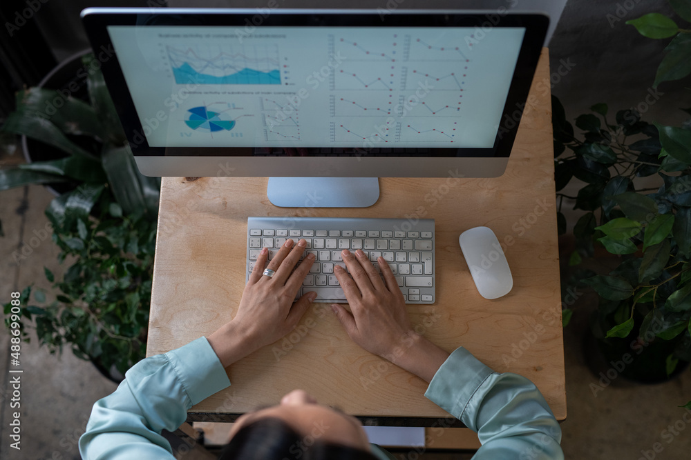 Aufkleber Overview of young female eonomist keeping her hands of computer keyboard while analyzing financial diagram and graphs