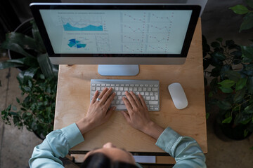 Overview of young female eonomist keeping her hands of computer keyboard while analyzing financial diagram and graphs