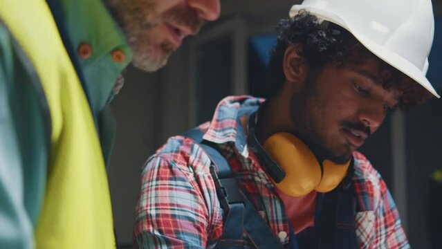Serious face two builders men in hardhats working talking in the evening light use blueprints during renovation in building. Portrait. Slow motion
