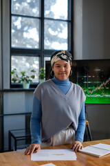 Young biracial businesswoman standing by table against interactive screen in boardroom while teaching colleagues at seminar