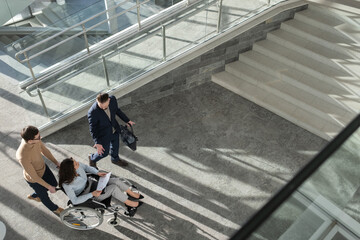 Above angle of confident ceo explaining business strategy to female colleague or partner with disability while moving along office center - obrazy, fototapety, plakaty