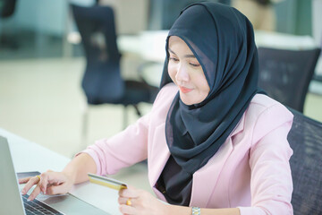 Portrait of a young Muslim businesswoman in an office, Young arabic woman in headscarf using laptop and credit card, shopping online concepts