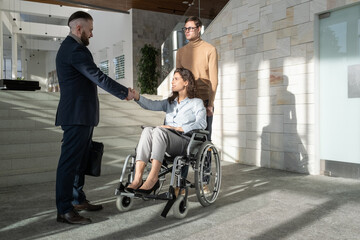 Young businesswoman with disability sitting in wheelchair while handshaking with partner after...