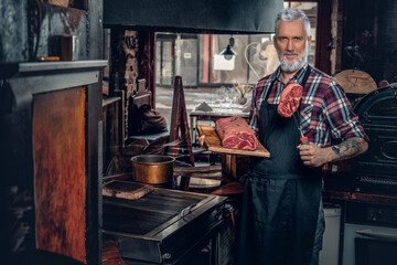 Fototapeta na wymiar Gray haired butcher and his job in old fashioned meat shop