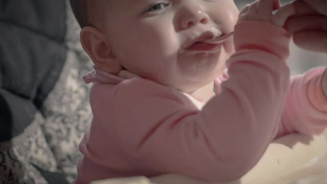 Baby Girl in High Chair Fed by Spoon Wearing Pink Bib