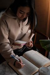 Shot of young asian female student sitting at table and writing on notebook. Young female student studying in cafe.