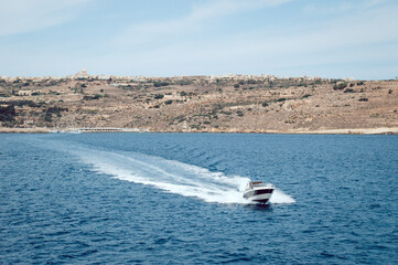Obraz premium The boat sails from the island into the sea leaving waves on the water