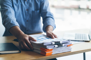 Businessman Preparing reports papers with graphs, charts on Stacks of documents files for finance in office. Piles unfinished achieves with paper clip near computer. Concept of Business Annual Report.