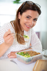 middle aged woman is eating vegetable salad at office desk