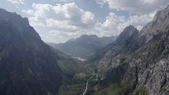 Frontal drone video descending between the hills of the Valbona valley, Albania, the beauty of nature and trees in the area can be seen.