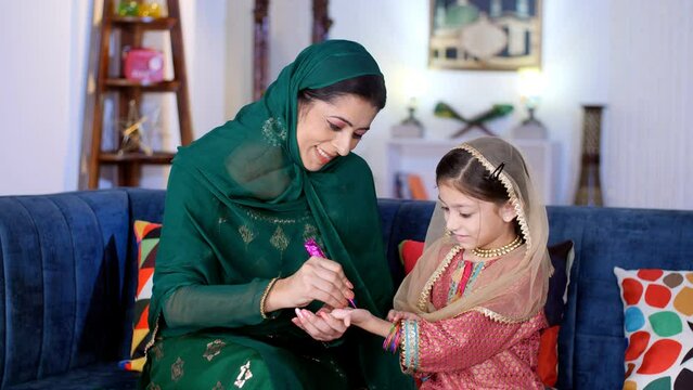 A pretty woman wearing a headscarf putting Mehendi / Henna on daughter's hand. A Muslim mother and her young girl - a beautiful design  parent-child bonding  leisure time  Muslim family  mother dau...