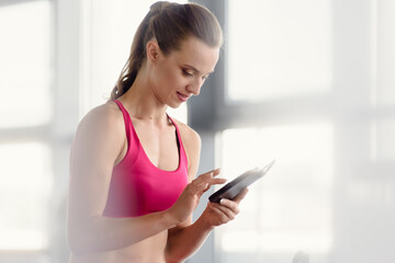 Beautiful athletic girl resting after training and using smartphone