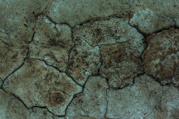 Texture of the dried earth. Dark green background with cracks and hollows. Drought and lack of moisture in the soil. The consequences of abnormal heat. Environmental disaster. Global warming.