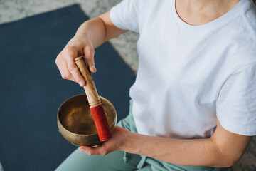 The girl meditates to the sounds of a Tibetan bowl, holds a stick in her hands to strike the sound....