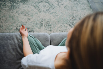 A view from above of a girl in the lotus position, meditating sitting on the couch in her house. The concept of Zen practice in the apartment. The hand of chin mudra.
