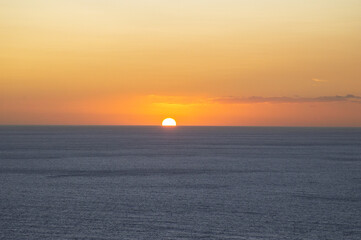 Half of the sun is visible above the horizon during sunset at sea