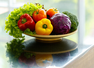 Closeup studio shot of variety freshness raw nutritional vegetable in basket plate on kitchen counter including green salad leaves tomatoes red and yellow sweet pepper purple cabbage and broccoli