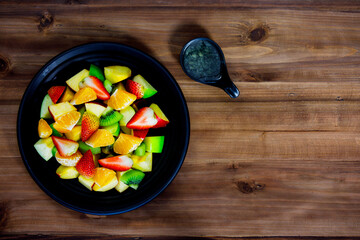 Top view shot of mixed sliced fresh raw healthy tasty fruits salad appetizer and dressing placed on wooden table with spoon fork decorated with sack napkin serving with tomato juice drink in glass