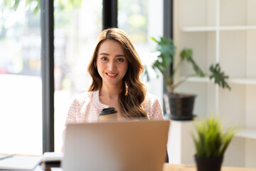 Portrait young attractive beautiful asia female sit on desk smile to camera work at home remotely computer laptop job. College student, employee feel cozy happy in weekend work life balance.