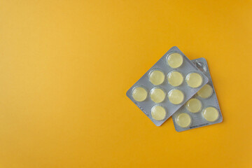 Two whole silver blister packs of yellow round cough drops. Yellow background. For sore throats and dry cough. Top view.