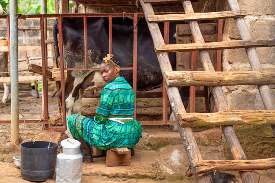 Young African woman seated next to cow shed 