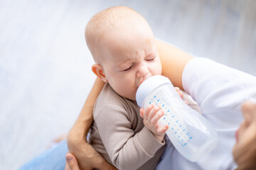 crying baby with a bottle of milk in mom's arms close-up