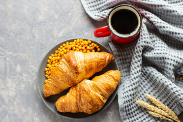 two croissants are on a gray plate and a mug of hot coffee are on a gray background,flat lay