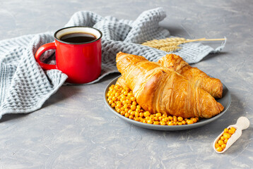 two croissants on a grey plate and a mug of hot coffee stand on a grey background, ready for breakfast