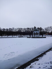 Winter snowy landscape in Kadriorg park. Frozen water in the pond. White wooden gazebo in the middle. Trees with no leaves on the back. Tallinn, Estonia, Europe. February 2022