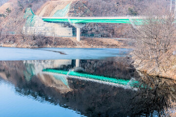 Green highway bridge over partially frozen river in rural countryside.