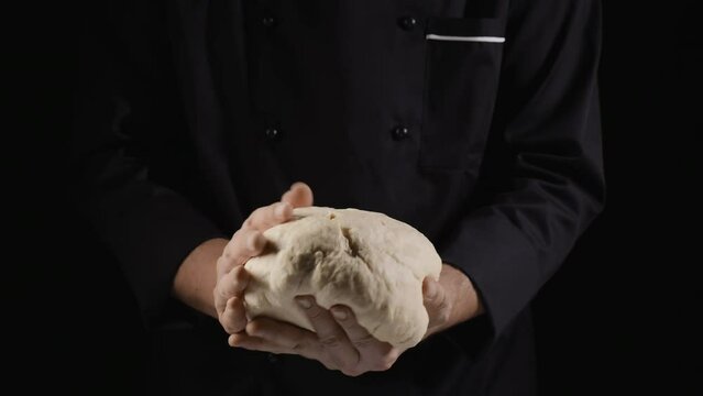 A baker dressed in a black suit forms a glob of dough, holding it in his hands, close-up shot. Prepares ecologically natural pastries