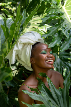Portrait of a smiling young African woman, in leaves, wearing a  headwrap