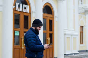 Urban portrait of young elegant business man in winter casual clothes, jacket, hat. Walking in the city street, talking on the phone, making selfie. Working outdoor