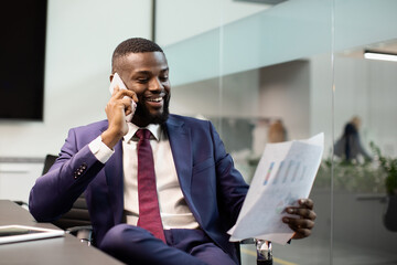 Smiling black entrepreneur having phone conversation at office, reading documents