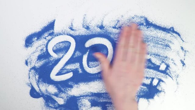 Write 2024 on blue sand year. Painting in the sand. Draw with your hands on the croup. Hand drawing. Erase text by hand. wash