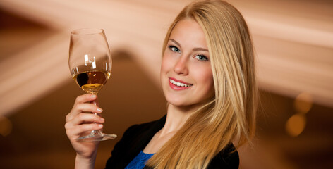 Beautiful young blond woman drinks red wine in wine cellar