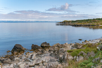Fototapeta na wymiar View of the coastline of the Isle of Islay with mainland Scotland on the horizon over clear calm blue sea water