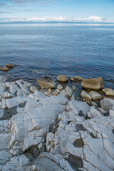 Rocks on the shore along the coast of the island of Islay with beautiful blue and clam water on a sunny summer day with mainland Scotland on the horizon