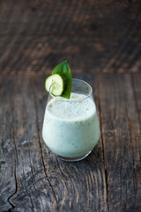 Green vegetable smoothie with almond milk and cucumber on a rustic wooden table. 