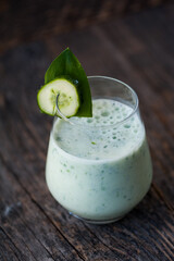 Green vegetable smoothie with almond milk and cucumber on a rustic wooden table. 