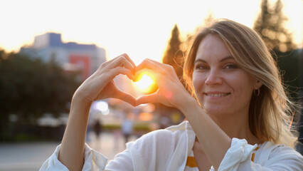 happy woman making a heart shape from her hands in the city on a sunny day during sunset