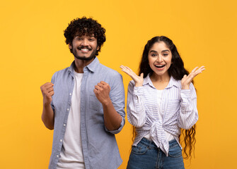 Wow. Overjoyed indian spouses gesturing in amazement looking at camera over yellow studio background