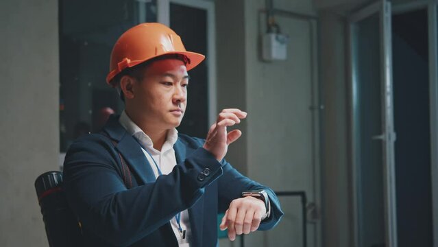 Asian architect engineer man in hardhats hand touching a smart watch scrolling in the air during renovation in building. Technology. For Holographic. Slow motion - Powered by Adobe