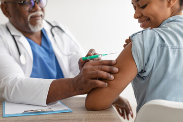 Black Woman Receiving Coronavirus Vaccine Injection Sitting With Doctor Indoor