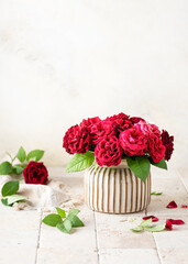 Beautiful bouquet of summer dark red roses in ceramic vase on light stone mosaic background. Floristic or home deco concept. Selective focus.