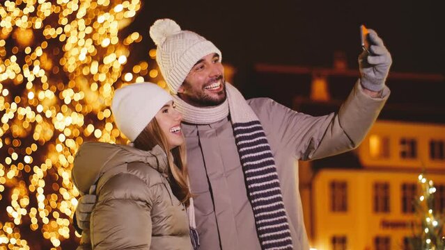 winter holidays, leisure and people concept - happy couple taking selfie with smartphone in city over christmas lights