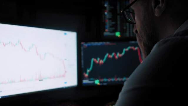 Bearded trader frustrated looks at a stock market monitor at a loss focus foreground slow motion