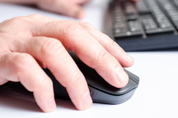 A computer mouse in a man's hand and a black keyboard. White background.
